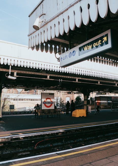 The image depicts the exterior of Guildford Station with a focus on the platform area beneath the canopy, showcasing a small group of people preparing for a home relocation. Visible are several cardbo